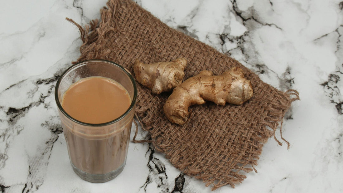 A glass of creamy tweak ginger chai placed on a rustic burlap cloth, accompanied by fresh ginger roots. The warm and comforting Indian chai ginger tea with ginger enhances immunity and provides a soothing experience. Buy ginger tea from Chai Hai.